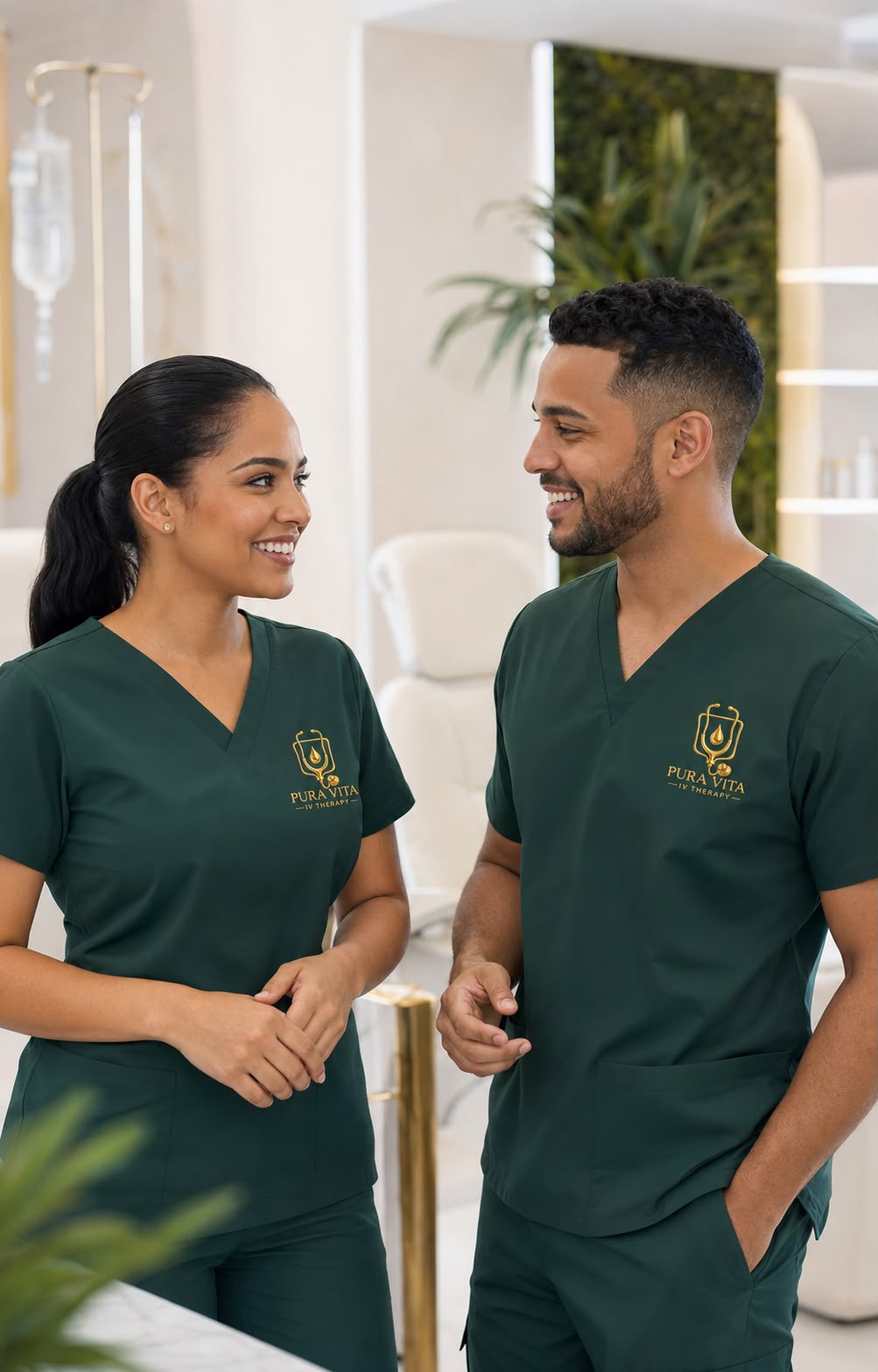 Dos profesionales de enfermería de Pura Vita IV Therapy con uniforme verde oscuro y logo dorado, conversando en la clínica